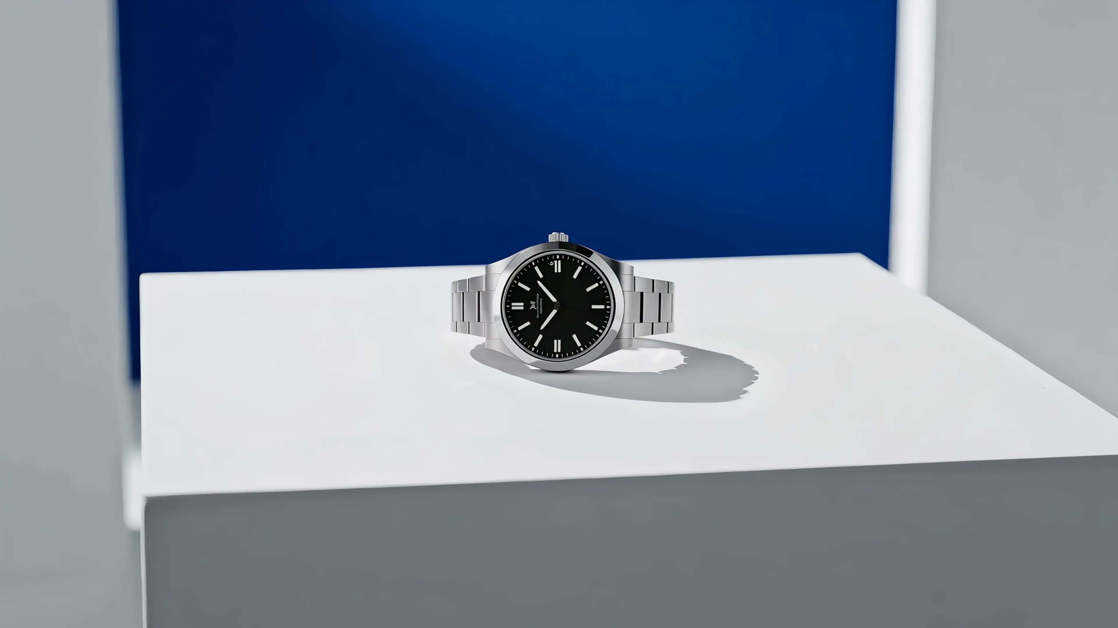A premium watch on a white studio pedestal with a cobalt accent panel